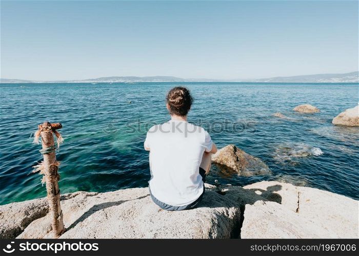 Young hipster man with a bum hair looking the ocean during a sunny day with a white tshirt, liberty and freedom concept