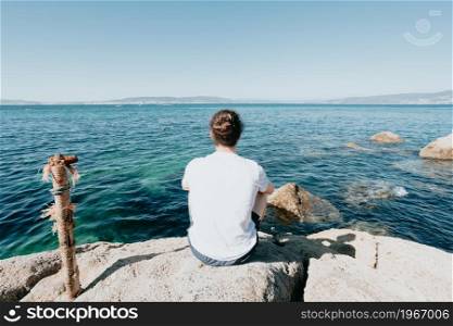 Young hipster man with a bum hair looking the ocean during a sunny day with a white tshirt, liberty and freedom concept