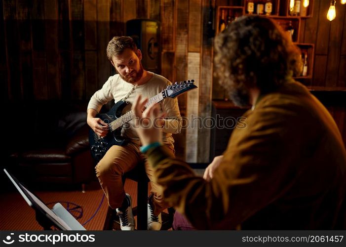 Young hipster musician guy teaching male student to play electric guitar at bar cafe. Musician teaching male student to play guitar