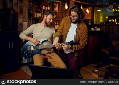 Young hipster musician guy teaching male student to play electric guitar at bar cafe. Musician teaching male student to play guitar