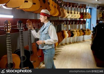 Young hipster woman choosing acoustic guitar in instrument shop. Female buyer at musical store. Young hipster woman buyer choosing acoustic guitar in instrument shop