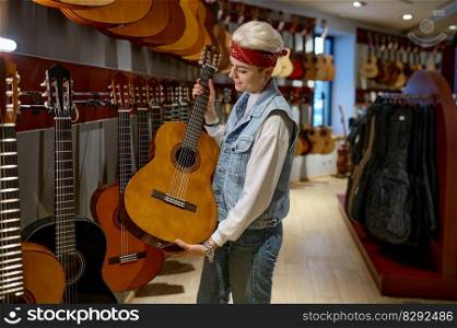 Young hipster woman choosing acoustic guitar in instrument shop. Female buyer purchasing at musical store. Young hipster woman buyer choosing acoustic guitar in instrument shop