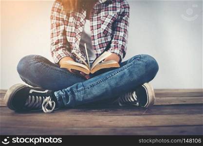 Young hipster woman holding open book sitting on wooden floor.