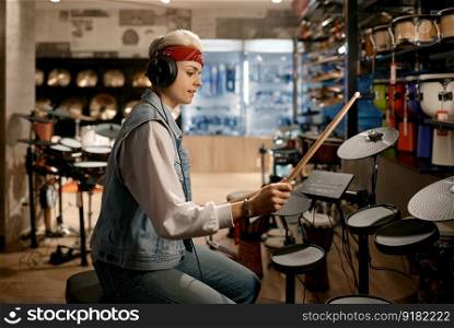 Young hipster woman musician wearing headphones playing electronic drum set at music instrument shop. Hipster woman musician wearing headphones playing drum set at music shop