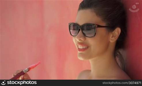Young hispanic people smoking e-cig, pretty sensual latina woman with electronic cigarette, happy sexy girl with sunglasses smiling and blowing smoke. Slow motion portrait