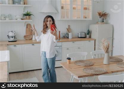 Young hispanic woman boasting with her stylish kitchen. Housewife has video phone call at home. Girl shows modern white scandinavian interior into camera. Stove, worktop and cuisine.. Young hispanic woman boasting with her stylish kitchen. Housewife has video phone call at home.