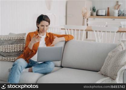 Young hispanic woman has online conference at home. Girl with laptop is talking at internet meeting. Pretty lady is sitting on sofa having discussion. Working while quarantine.. Young hispanic woman has online conference at home. Lady is sitting on sofa having discussion.