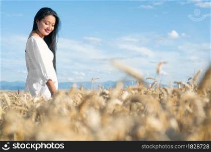 Young Hispanic woman in white dress walking in the middle of a wheat field smiling. High quality photography.. Young Hispanic woman in white dress walking in the middle of a wheat field smiling.