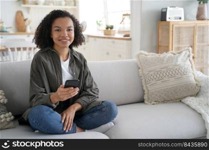 Young hispanic woman is browsing social media and smiling. Curly african american girl has fun with phone at home. Chatting with friends remotely. Lazy weekend morning. Online book reading.. Young hispanic woman is browsing social media. Online book reading. Lazy weekend morning.