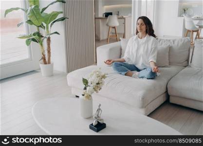 Young hispanic woman is practicing yoga and meditation in morning at home. Girl is doing posture exercise, sitting in lotus asana. Morning gymnastics. Body care, fitness and wellbeing concept.. Young hispanic woman is practicing yoga in morning at home. Body care, fitness and wellbeing.