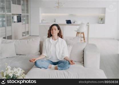 Young hispanic woman is practicing yoga and meditation on couch at home. Posture exercise, lotus asana. Morning gymnastics, healthy lifestyle. Concentration and zen finding concept.. Young hispanic woman in practicing yoga and meditation on couch at home. Zen finding.