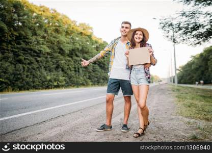 Young hitchhiking couple with empty cardboard. Hitchhike adventure of man and woman. Happy hitchhikers on road. Young hitchhiking couple with empty cardboard