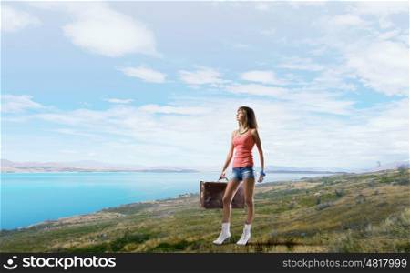 Young hitchhiking traveler. Young pretty girl walking with her retro suitcase in hand