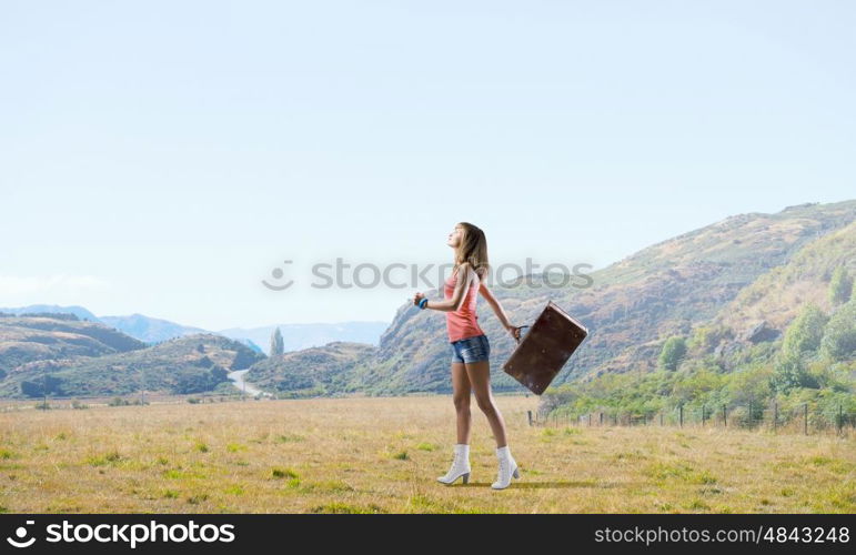 Young hitchhiking traveler. Young pretty girl walking with her retro suitcase in hand