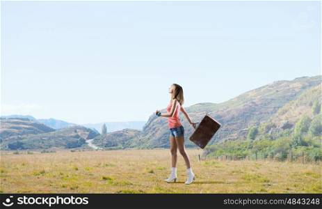 Young hitchhiking traveler. Young pretty girl walking with her retro suitcase in hand