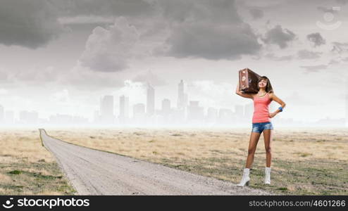 Young hitchhiking traveler. Young pretty girl with her retro suitcase on shoulder