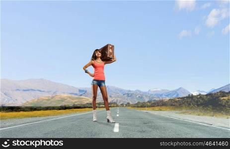 Young hitchhiking traveler. Young pretty girl with her retro suitcase on shoulder