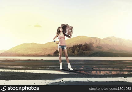 Young hitchhiking traveler. Young pretty girl with her retro suitcase on shoulder