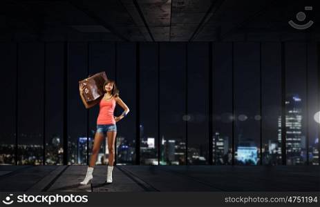 Young hitchhiking traveler. Young pretty girl with her retro suitcase on shoulder at night