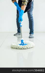 Young housekeeper cleaning floor mobbing holding mop and plastic bucket with brushes, gloves and detergents in the leaving room house floor helping his wife