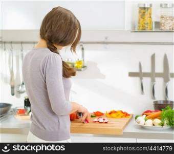 Young housewife cutting vegetables on salad in kitchen. rear view