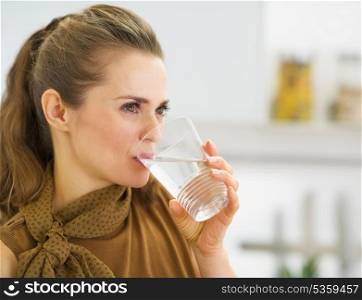 Young housewife drinking water in kitchen