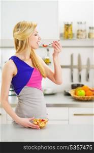 Young housewife eating fruits salad in kitchen