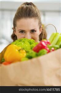 Young housewife hiding behind shopping bag full of vegetables