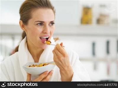 Young housewife in bathrobe having healthy breakfast in kitchen