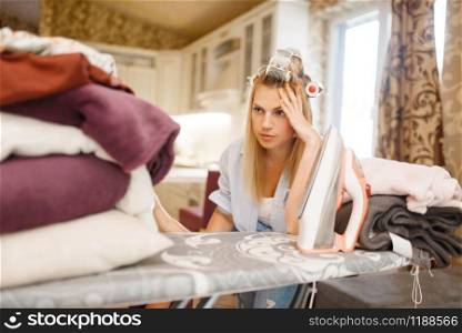 Young housewife sitting at the ironing board. Tired woman doing housework at home. Female person irons the clothes in the house