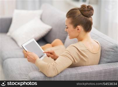 Young housewife sitting on couch using tablet pc . rear view
