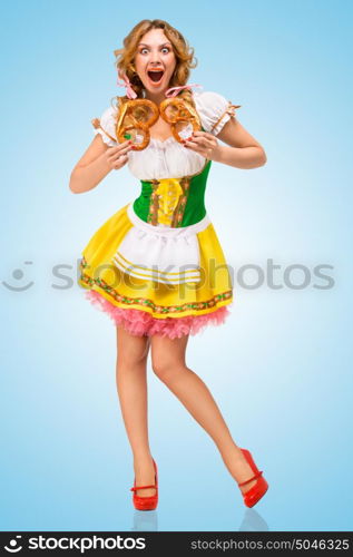 Young hungry sexy Oktoberfest woman wearing a traditional Bavarian dress dirndl holding two pretzels, and screaming on blue background.