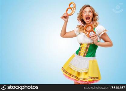 Young hungry sexy Oktoberfest woman wearing a traditional Bavarian dress dirndl holding two pretzels on blue background.