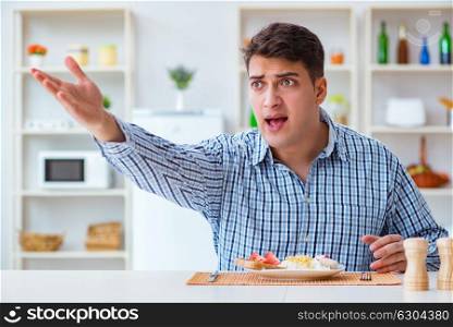 Young husband eating tasteless food at home for lunch