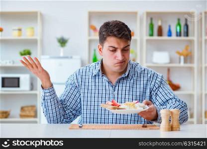 Young husband eating tasteless food at home for lunch