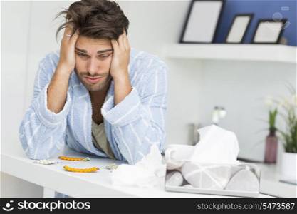 Young ill man suffering from headache at kitchen counter