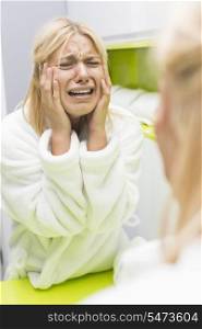 Young ill woman crying while looking at mirrior in bathroom