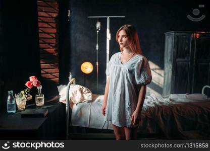 Young ill woman in the hospital, drip and bed on background. Illness of female patient in clinic, health recovery and treatment. Ill woman in hospital, drip and bed on background
