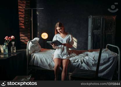Young ill woman sitting on hospital bed and reading book. Sick female patient in clinic. Ill woman sitting on hospital bed and reading book