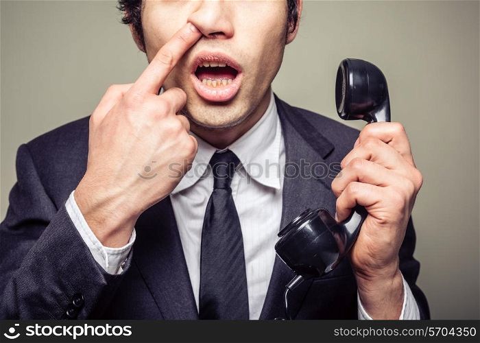 Young incompetent businessman is on the phone and is picking his nose