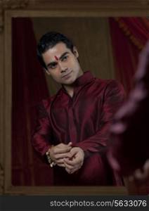 Young Indian bridegroom looking at self in mirror while getting dressed