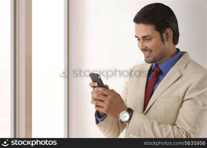Young Indian businessman reading text message through smart phone in office