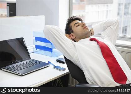 Young Indian businessman relaxing in chair at office
