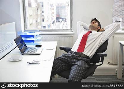Young Indian businessman relaxing in chair at office desk