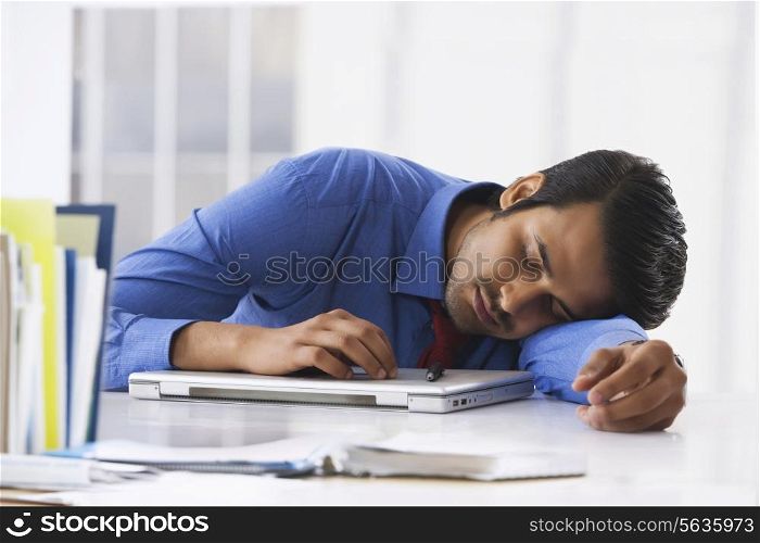 Young Indian businessman sleeping on laptop at office desk
