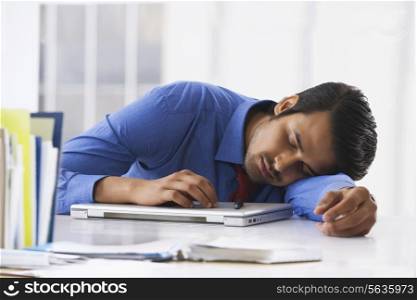 Young Indian businessman sleeping on laptop at office desk