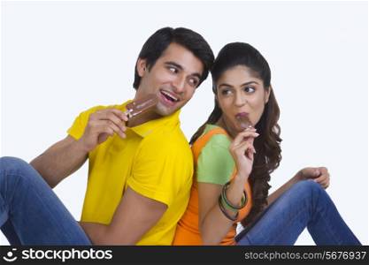 Young Indian couple eating chocolate ice-cream bars over white background