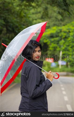 Young Indian girl with short hair holding a transparent umbrella and looking back, Pune. Young Indian girl with short hair holding a transparent umbrella and looking back, Pune.