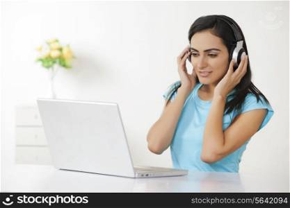 Young Indian woman listening to headphones in front of laptop at home