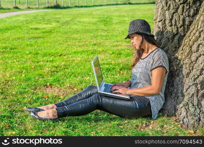 Young indian woman working with computer on lap at tree in nature